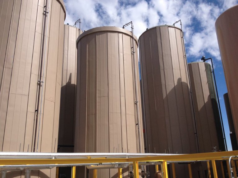 Row of large tan-coated storage tanks with yellow safety railing in the foreground