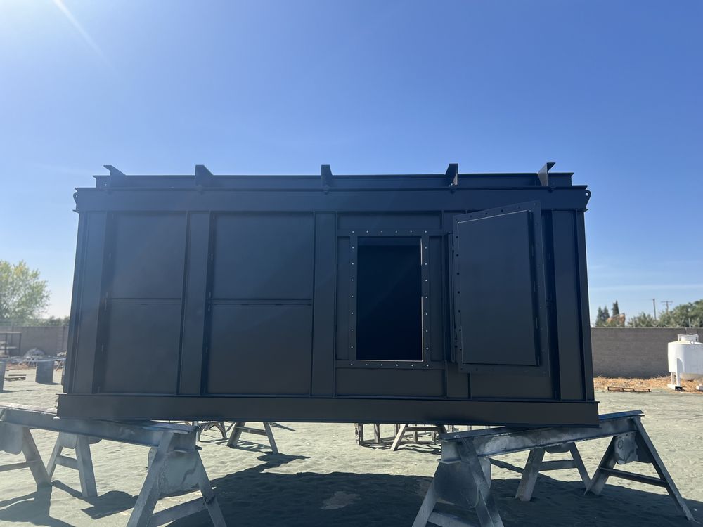 Large fabricated steel enclosure finished in a black industrial coating on sawhorses