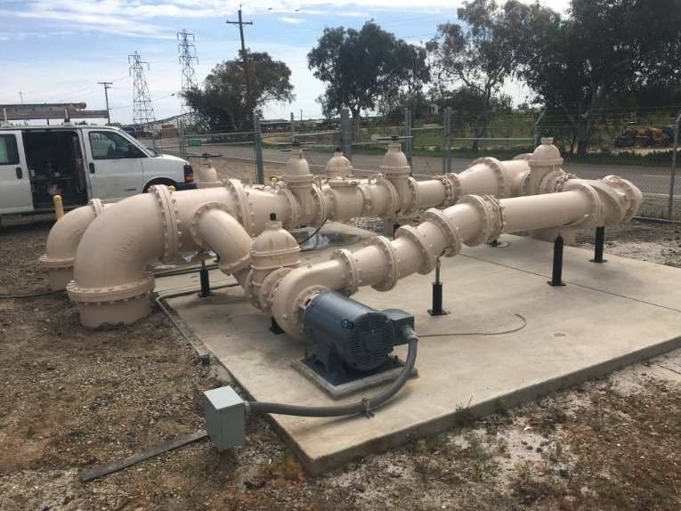 Coated tan pump station piping, valves, and motor on a concrete pad