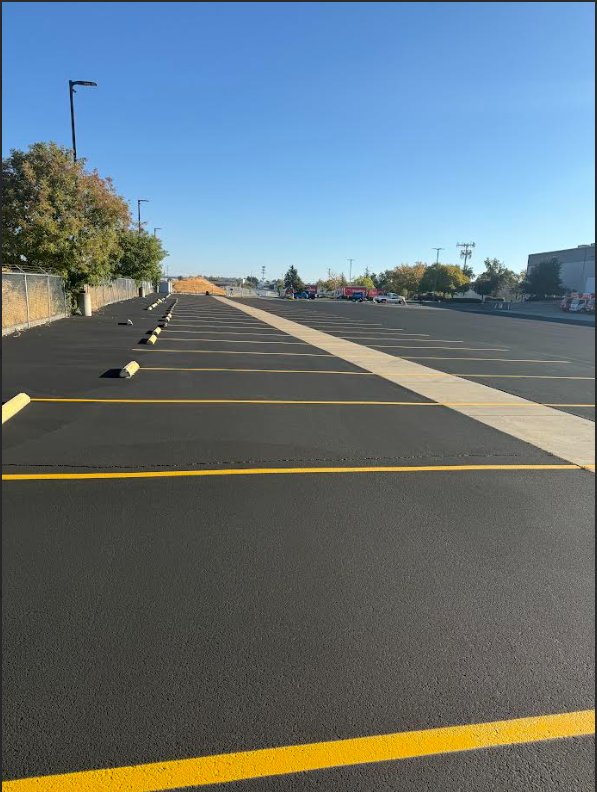 Freshly sealed asphalt parking lot with bright yellow stall striping and painted wheel stops