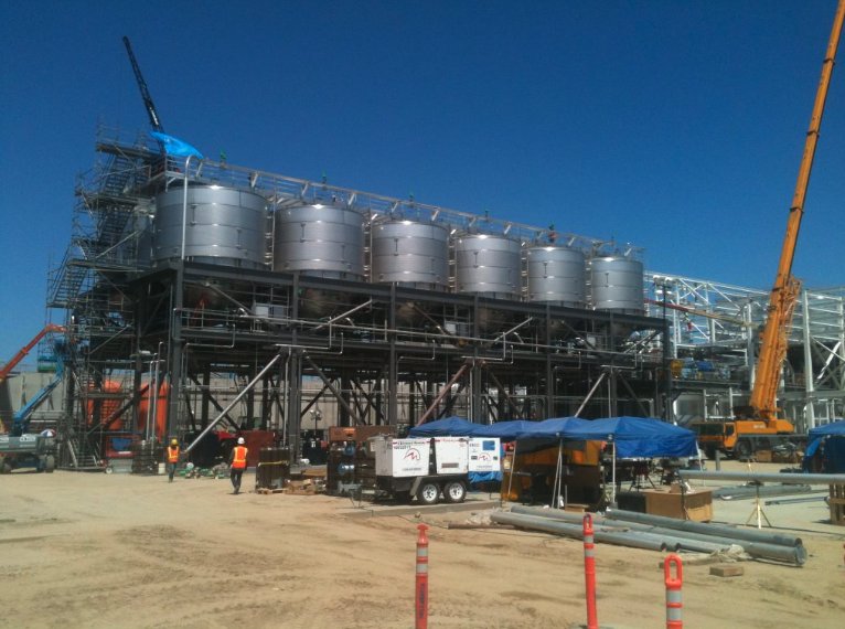 Bank of large stainless process tanks on structural steel framing under construction with crane on site