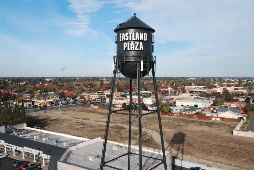 Restored Eastland Plaza water tower coated black with white lettering above a shopping center
