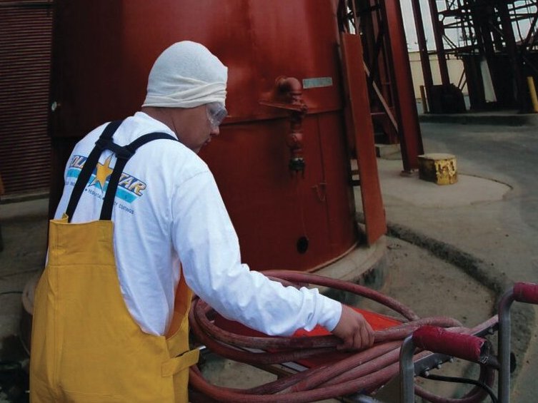 Gold Star Painting technician in protective gear handling spray hose beside a red-coated tank